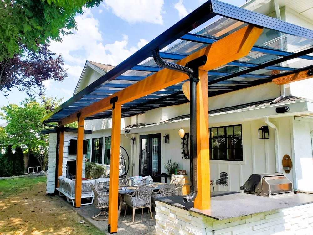 Outdoor deck with clear roof and wooden posts Outdoor covered deck with clear roof supported by wooden posts and black framing, furnished with dining table and grill.