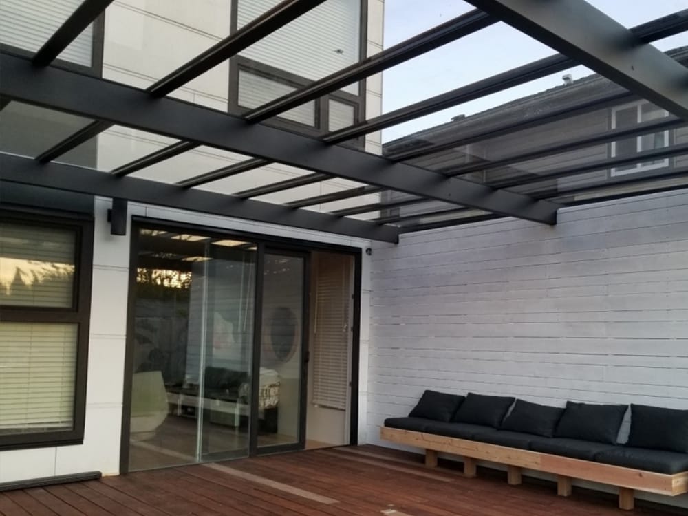 Glass roof patio with modern bench seating Modern patio with glass roof extension featuring black steel beams, sliding glass doors, and built-in wooden bench seating.